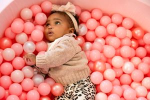 Young child playing in large pink ball pit filled with soft plastic spheres.