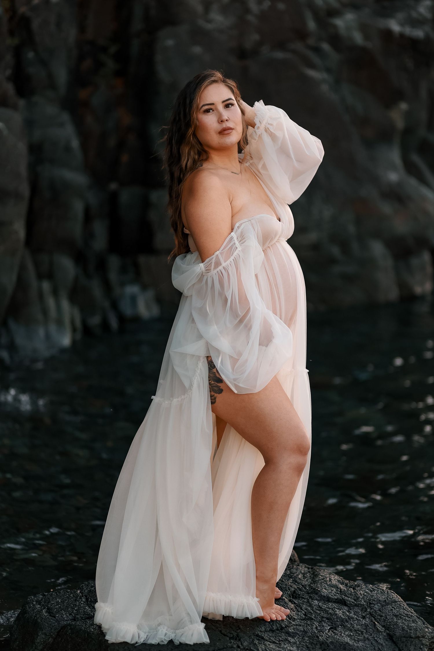 Ethereal white dress photographed against dark rocks near water.