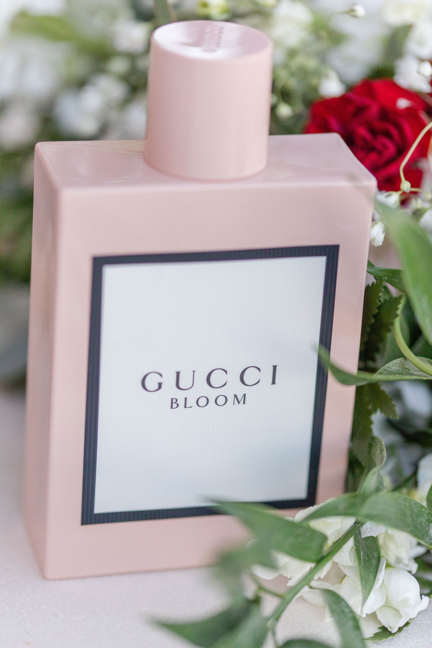 Pink Gucci Bloom perfume bottle styled with red roses and floral accents.