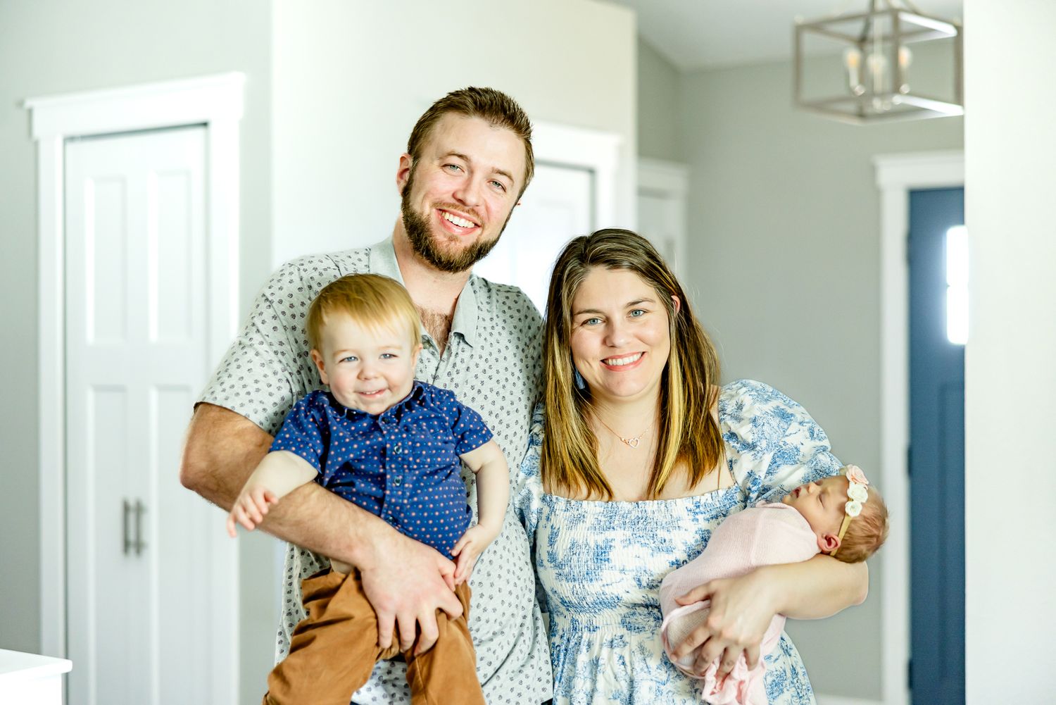 Parents smile holding their toddler boy and new baby girl during lifestyle newborn photos in Colorado Springs.