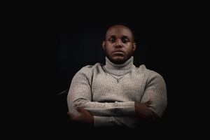 Figure in turtleneck sweater with arms crossed in studio portrait.