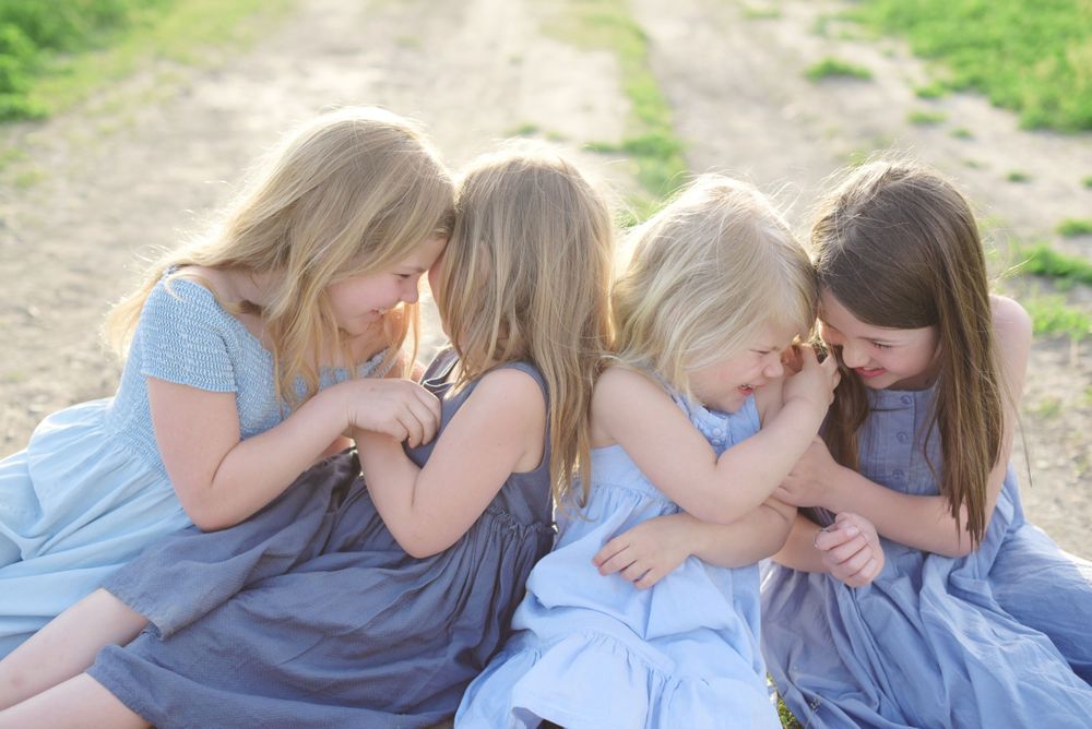 Four children in blue dresses share secrets and whispers while sitting together in Kelowna, B.C.