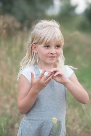 Young child in gray overalls gesturing playfully outdoors in a field in Penticton, B.C.