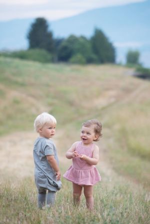Branding photos of two small children in casual wear playing together on a grassy hillside in Penticton, B.C.