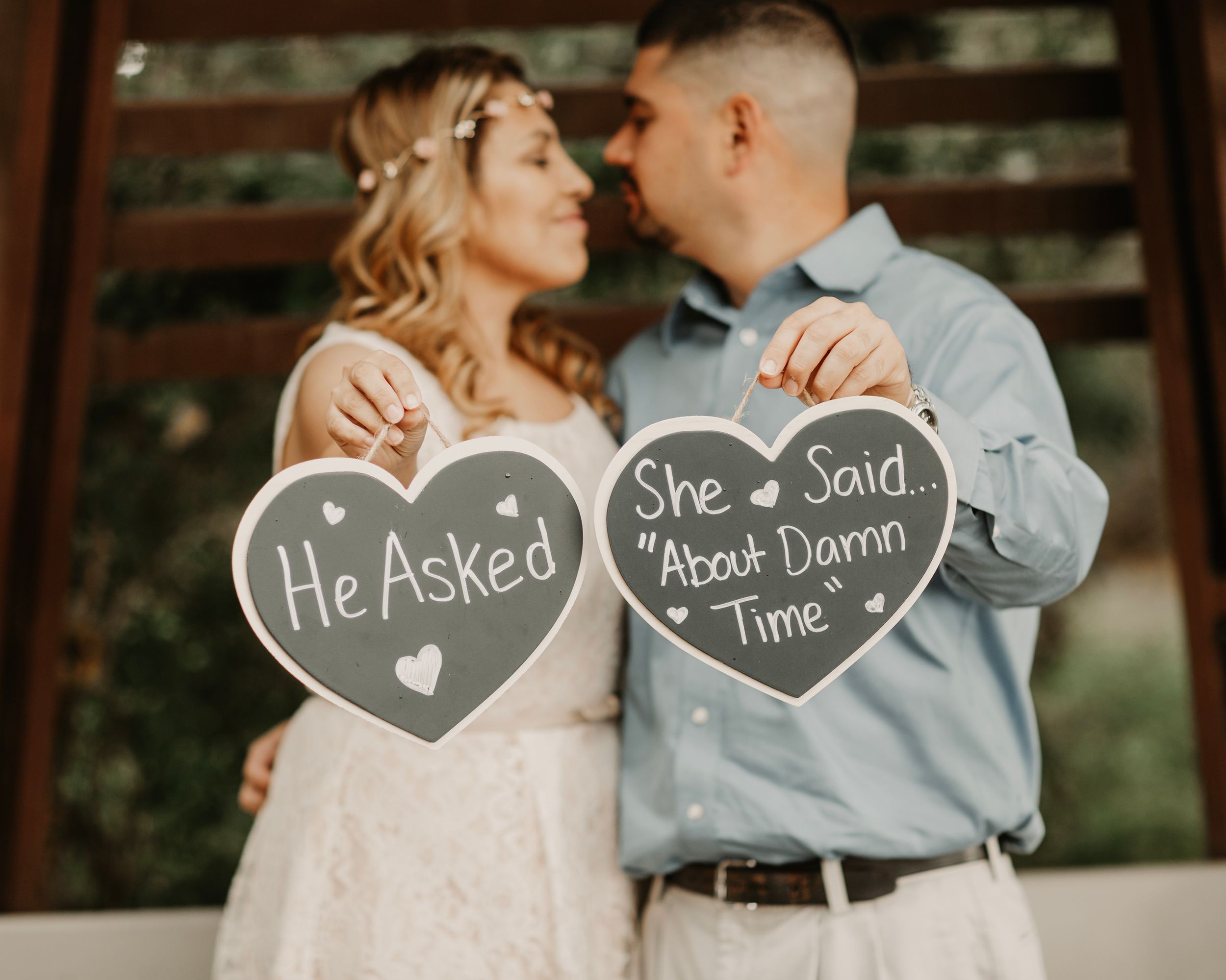 A romantic couple's photoshoot with heart-shaped chalkboard signs against a natural outdoor backdrop.