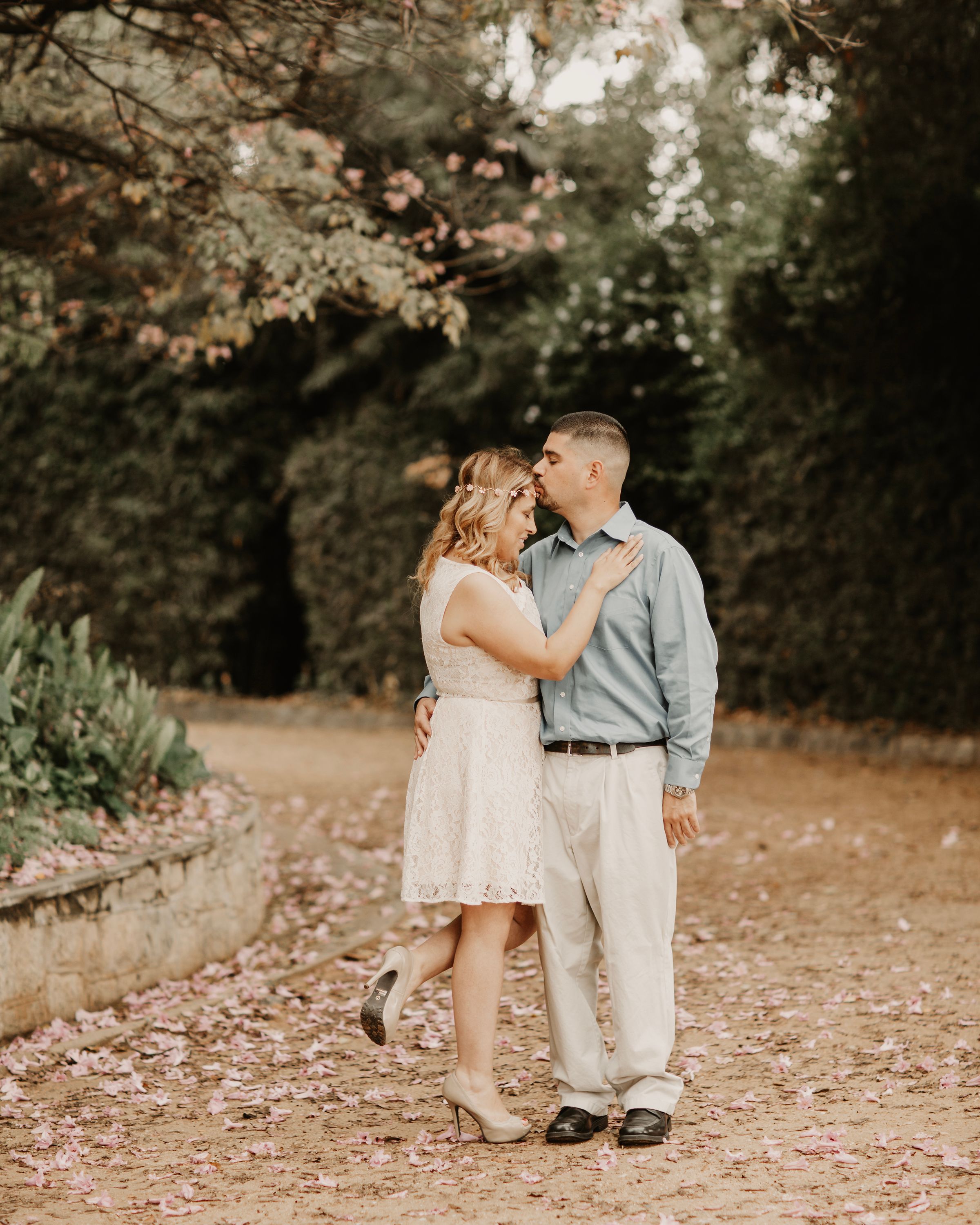 Romantic outdoor photoshoot with couple walking on path covered in fallen pink petals.