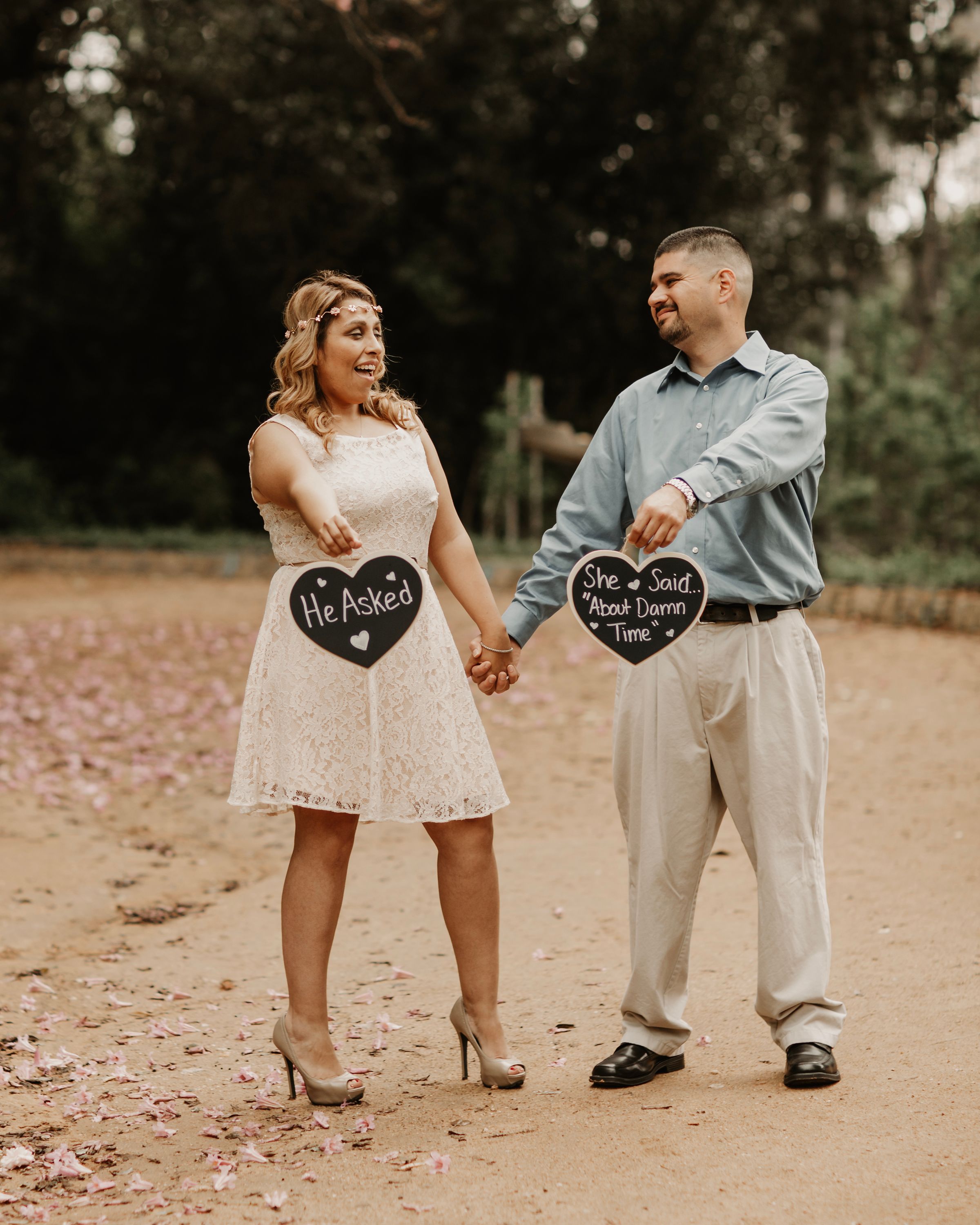 Couple displaying heart-shaped chalkboard signs during outdoor photoshoot on dirt path.