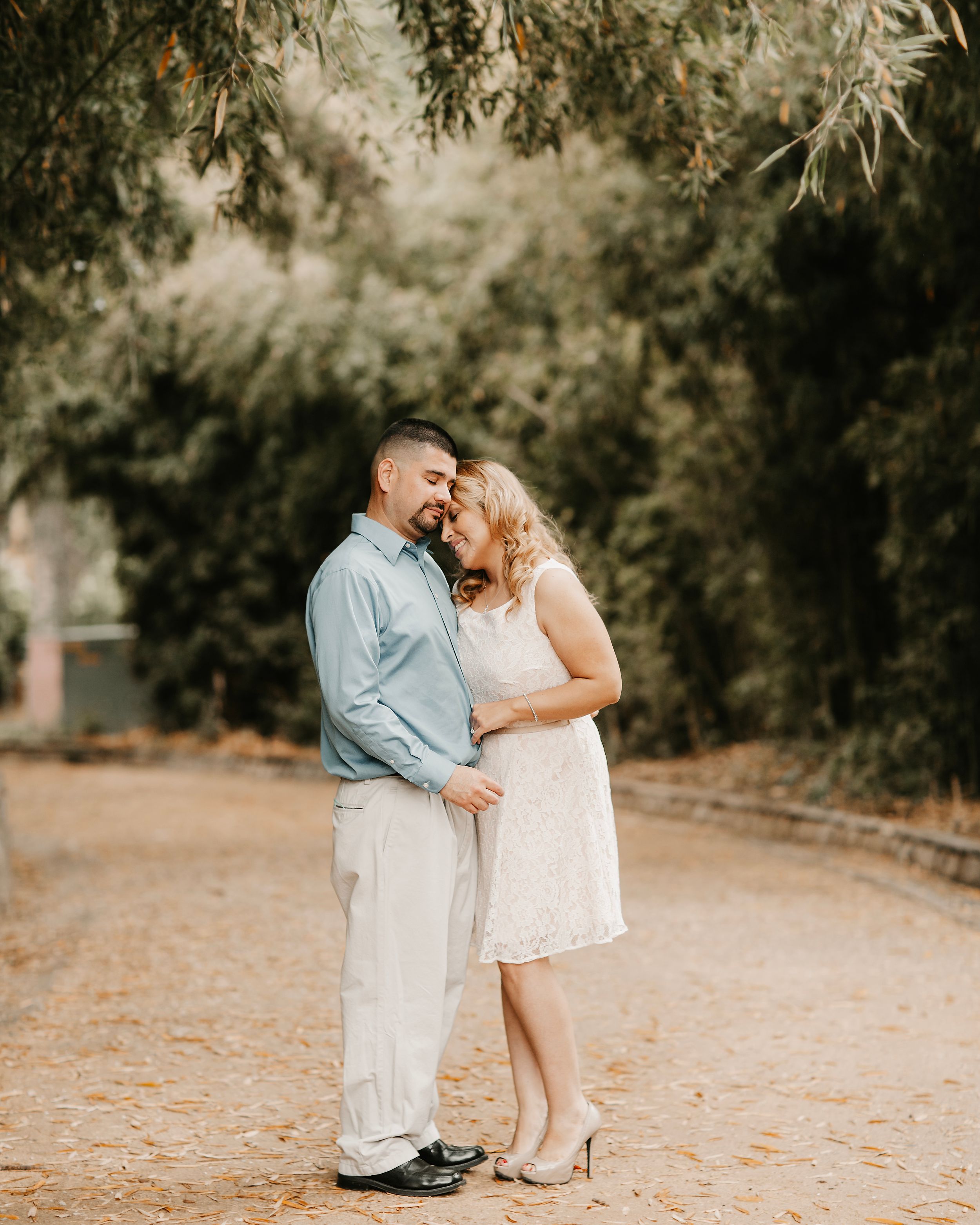 Romantic outdoor photoshoot with couple embracing under trees on dirt path.
