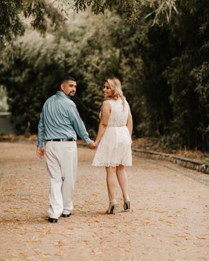 Couple walking together during sunset photoshoot on tree-lined dirt path.