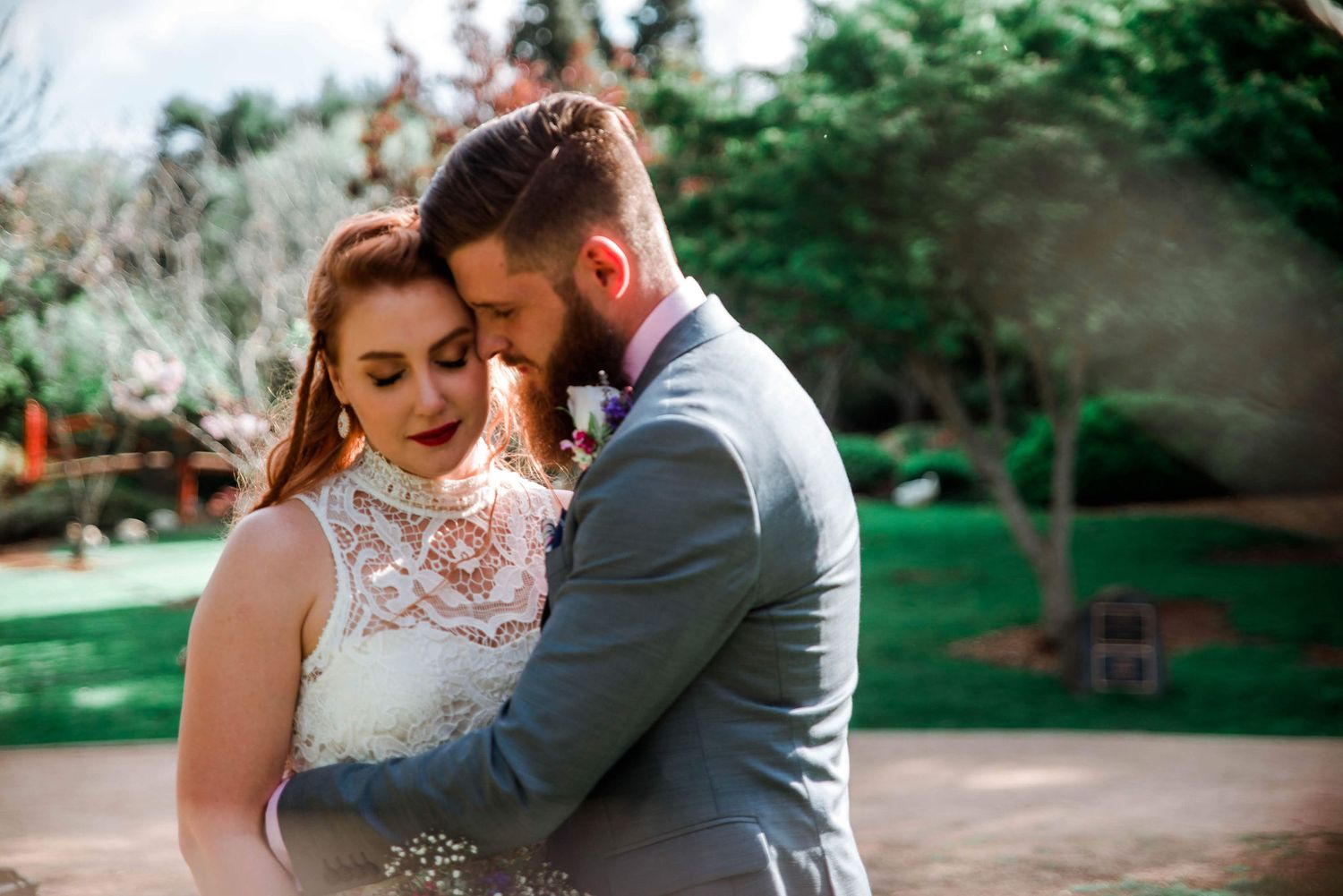 Tender wedding moment in garden setting with lace dress and grey suit details.