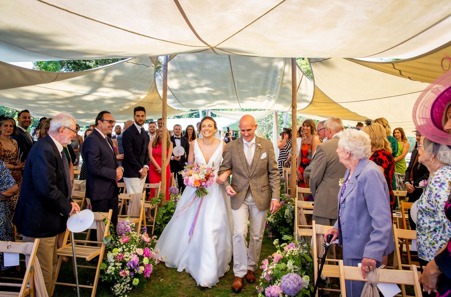 Wedding ceremony under sail cloth tents with floral decorations and seated guests.