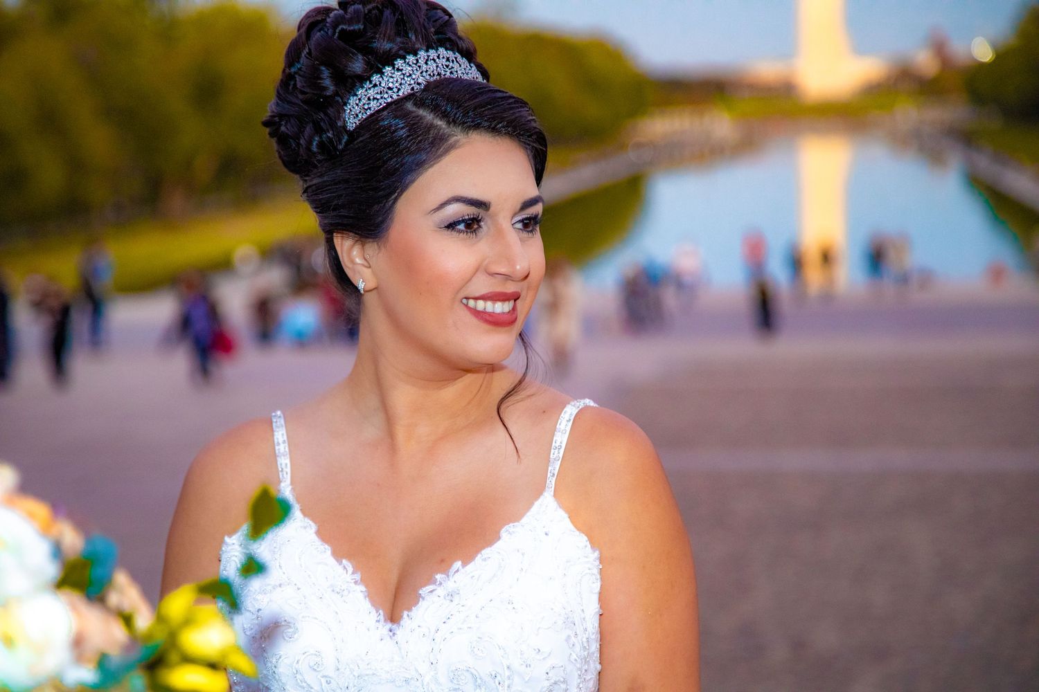 A radiant bride in a white dress and tiara poses in front of the Washington Monument at sunset.