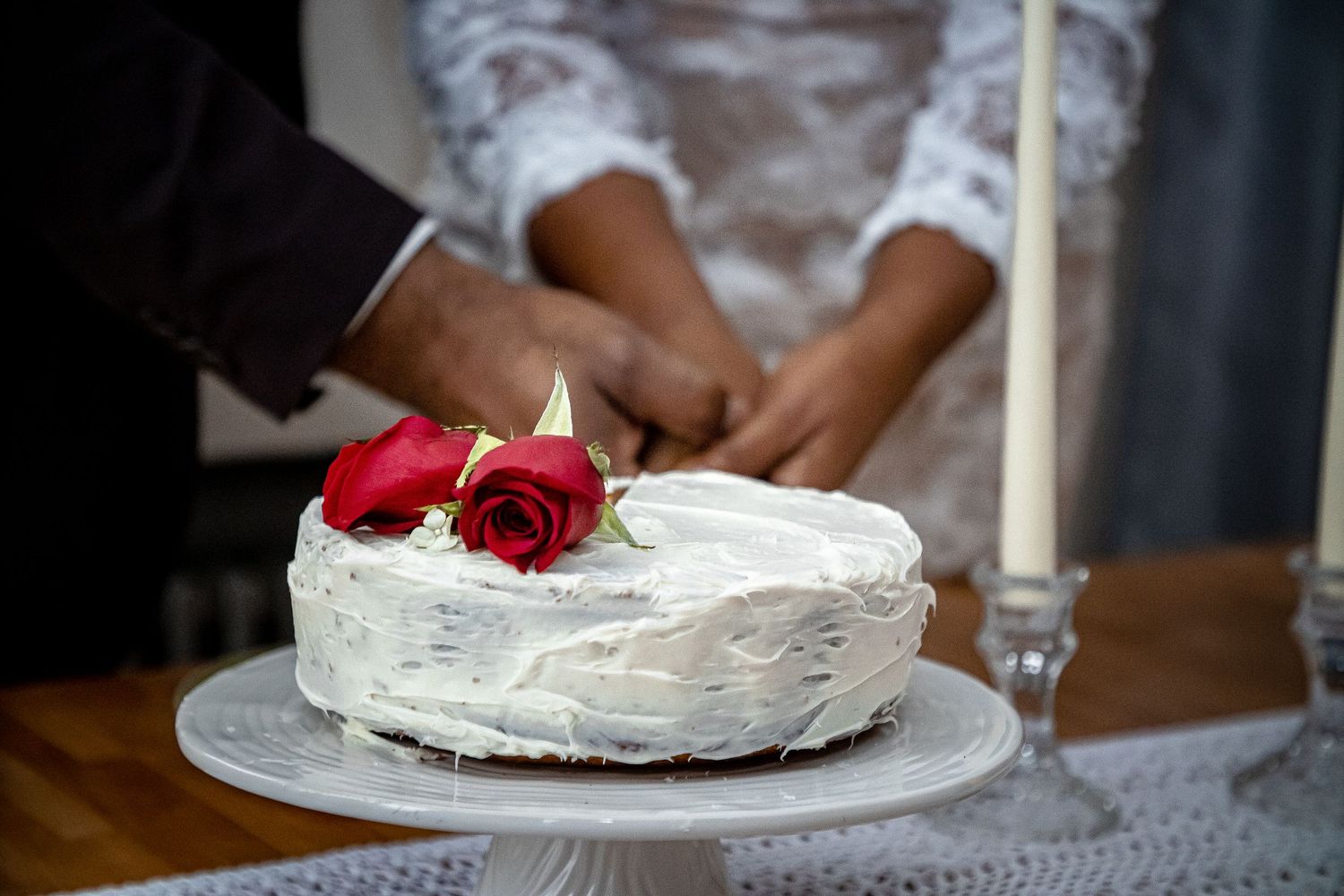White wedding cake decorated with red roses and lit candle on wooden table.