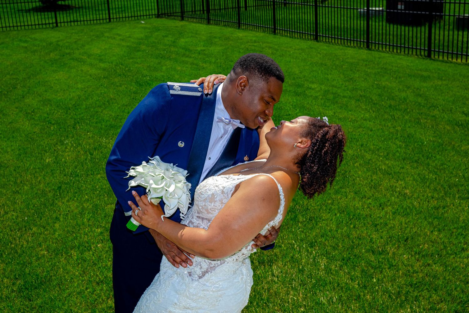 A romantic dip kiss on a green lawn during wedding photographs.