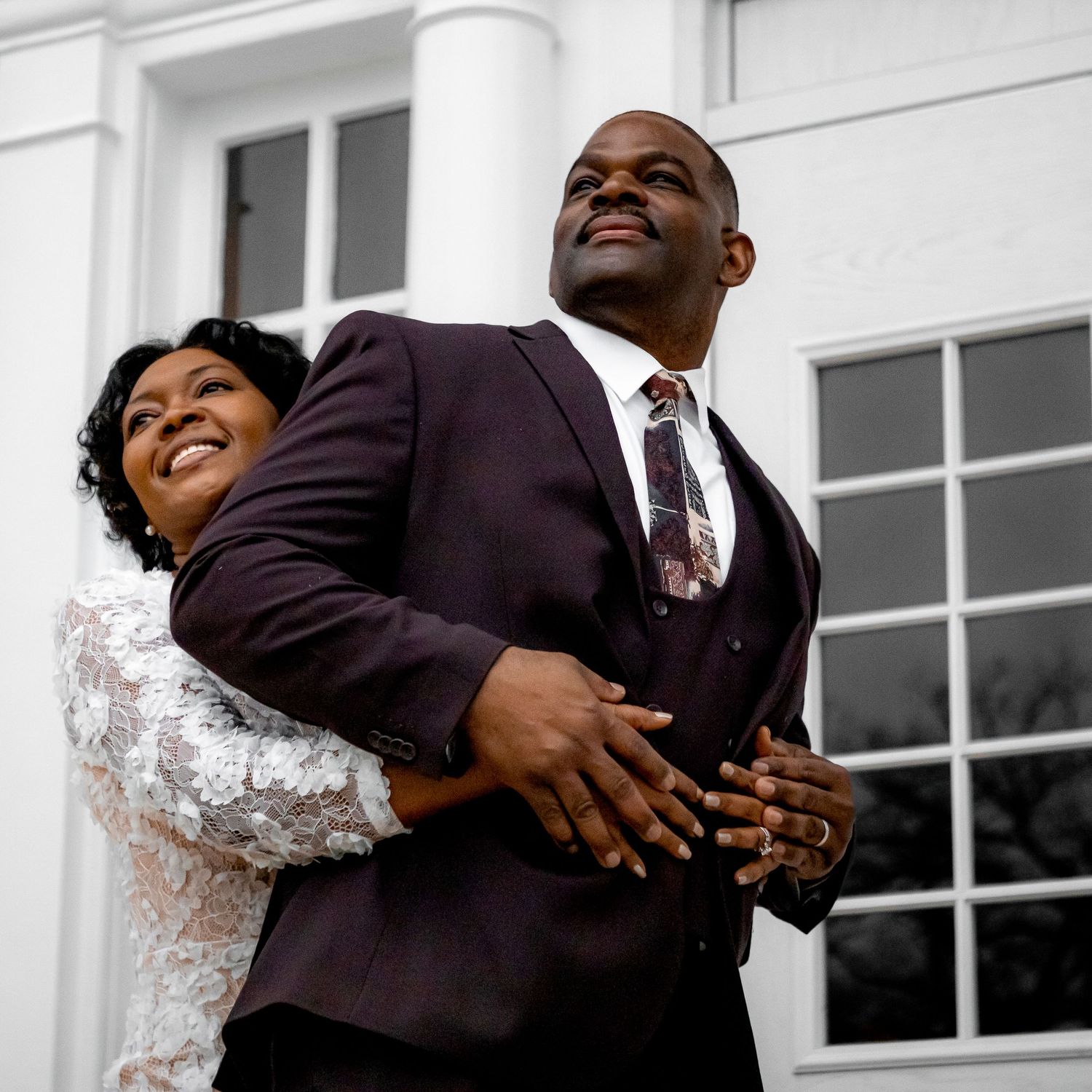 A happy couple embraces and smiles in front of a white columned building.