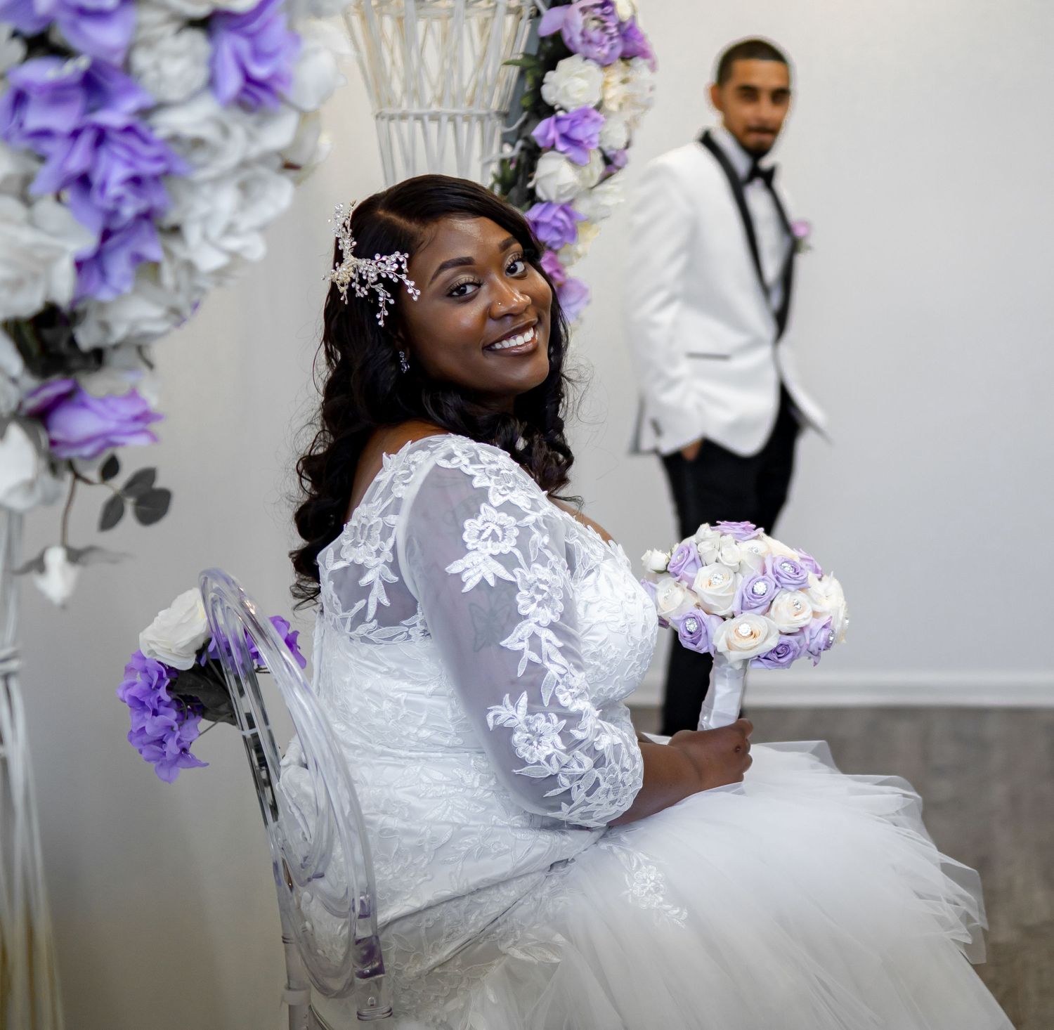 Bride posing with purple bouquet against floral arch during wedding photoshoot.