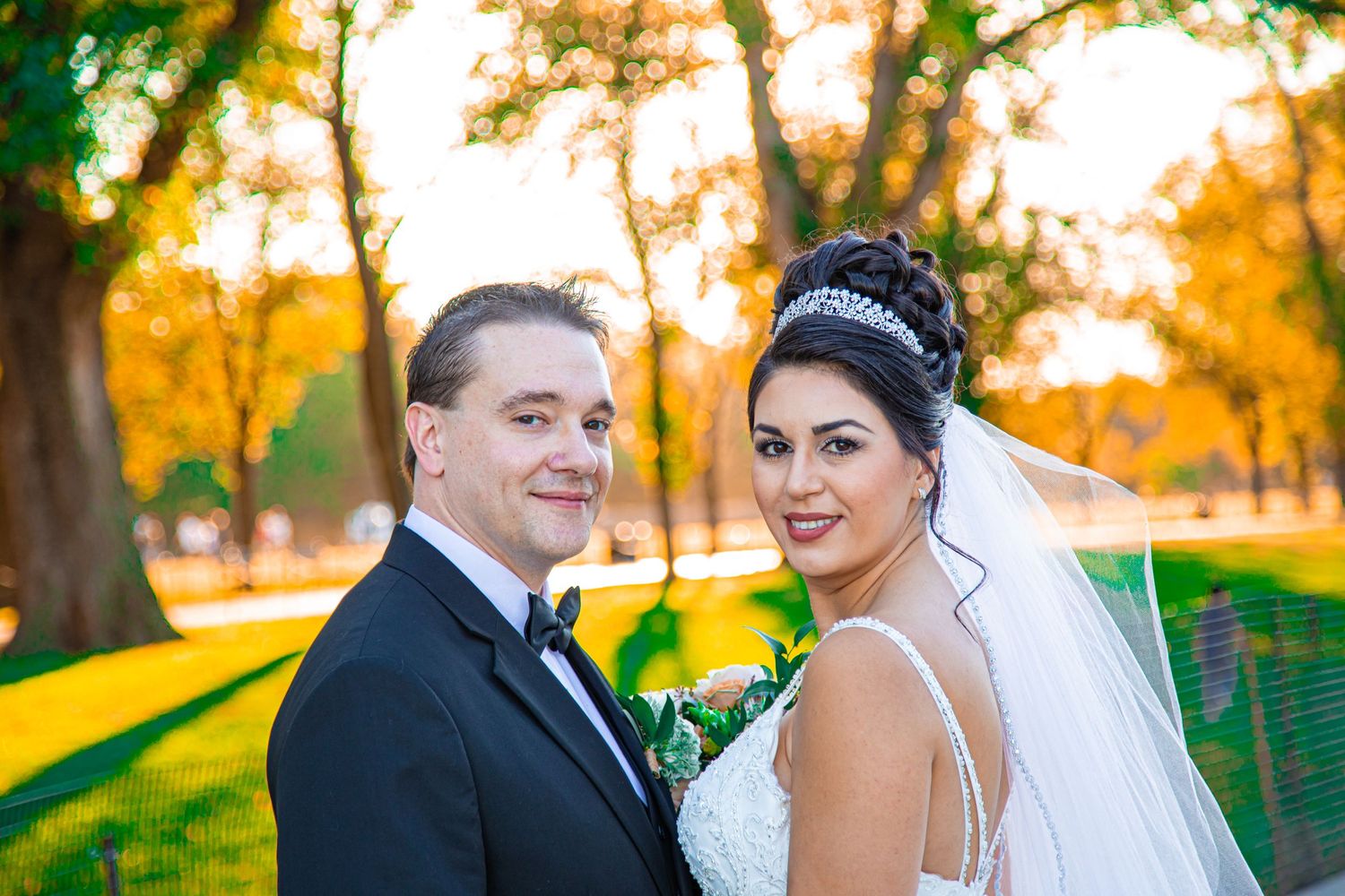 Newlywed couple smiling together in autumn park setting with golden sunlight.
