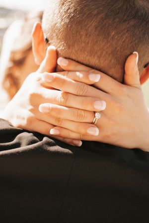 Close-up of hands with an engagement ring embracing at the neck during an intimate moment.