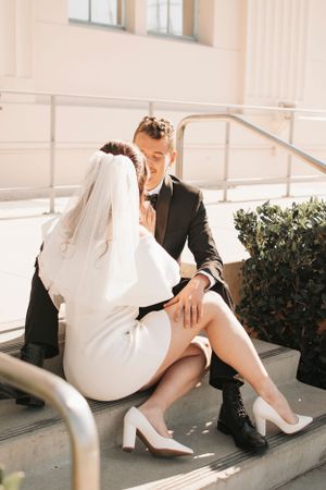 Couple in wedding attire sharing a romantic moment on outdoor steps.