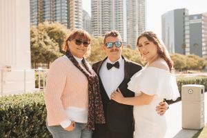 Wedding party poses with city skyline backdrop on sunny day.