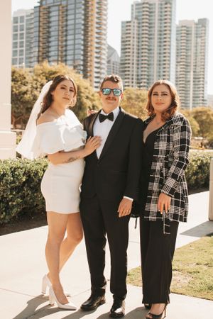 Wedding group photo with formal attire against modern urban backdrop.