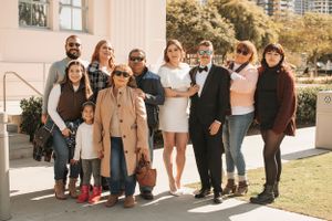 Large wedding party group photo outside building with modern architecture.