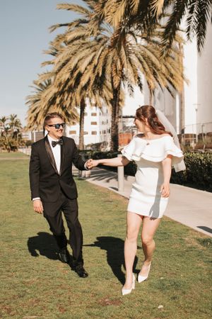 Playful wedding photo with palm trees and couple dancing on lawn.