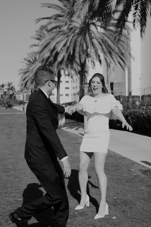 Black and white photo of couple dancing by palm trees in formal wedding attire.