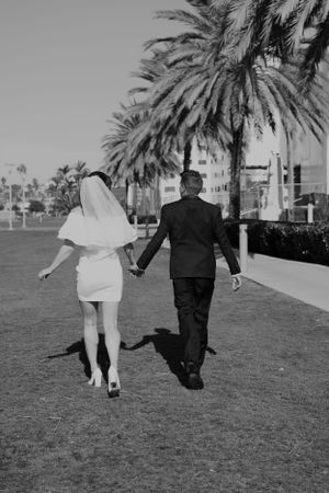 Elegant black and white shot of a couple walking on grass with palm trees in the distance.