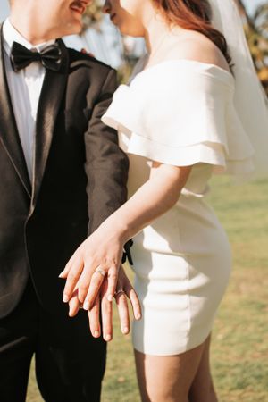 Bride in modern white dress and groom in tuxedo embrace during outdoor photoshoot.