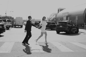 Black and white image of people crossing a street with vintage cars in background.