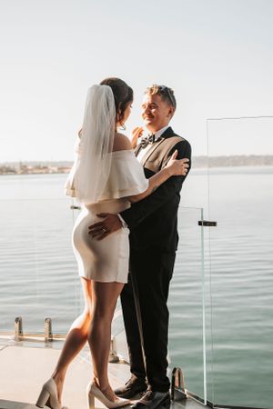Waterfront wedding photo with couple embracing on dock overlooking calm waters.