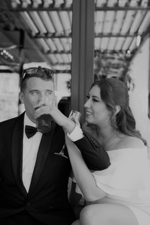 A playful black and white wedding moment shows a couple sharing a lighthearted interaction under a covered patio.