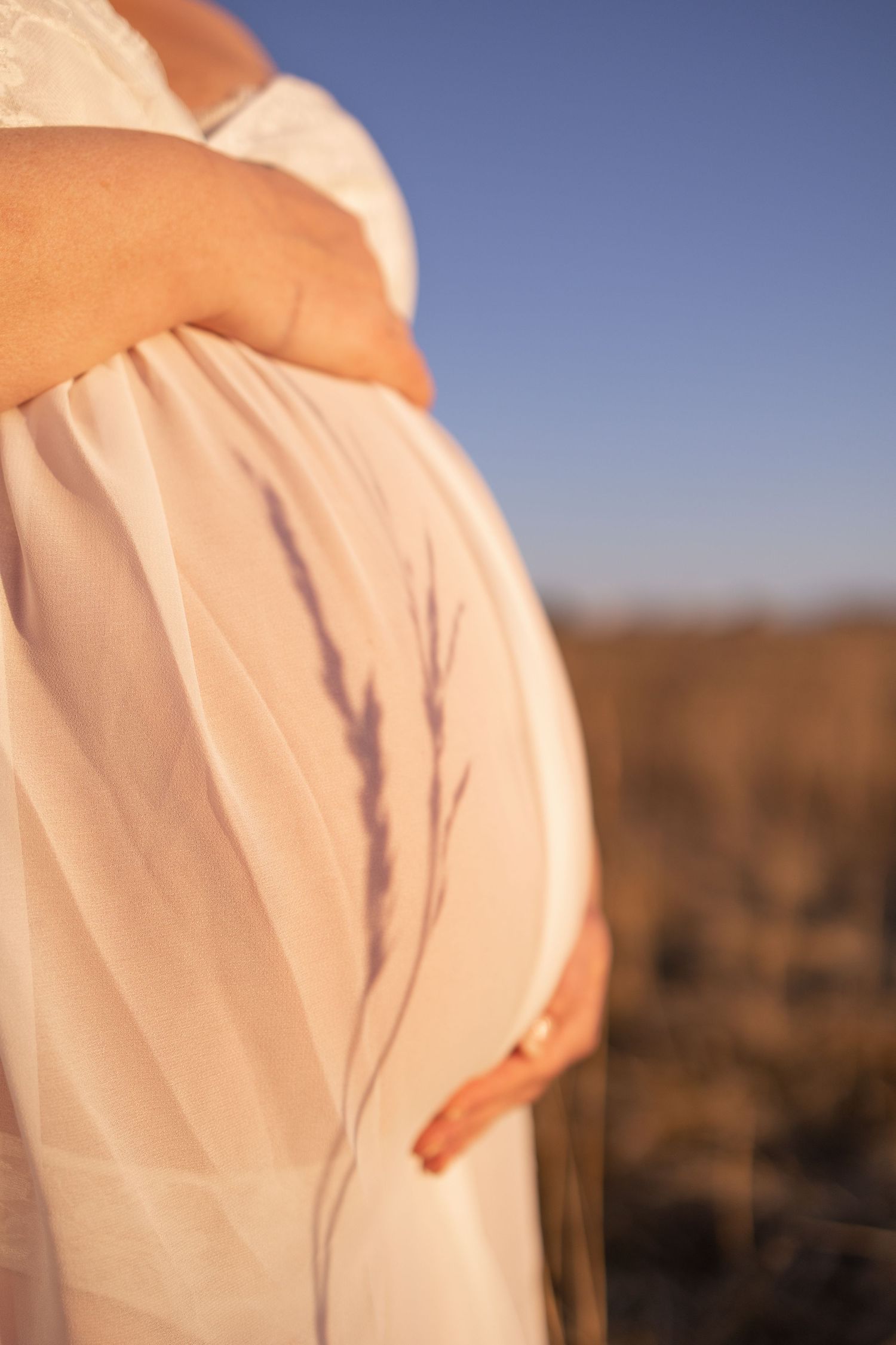 Side view of a pregnant belly wrapped in soft white fabric against a blue sky background.