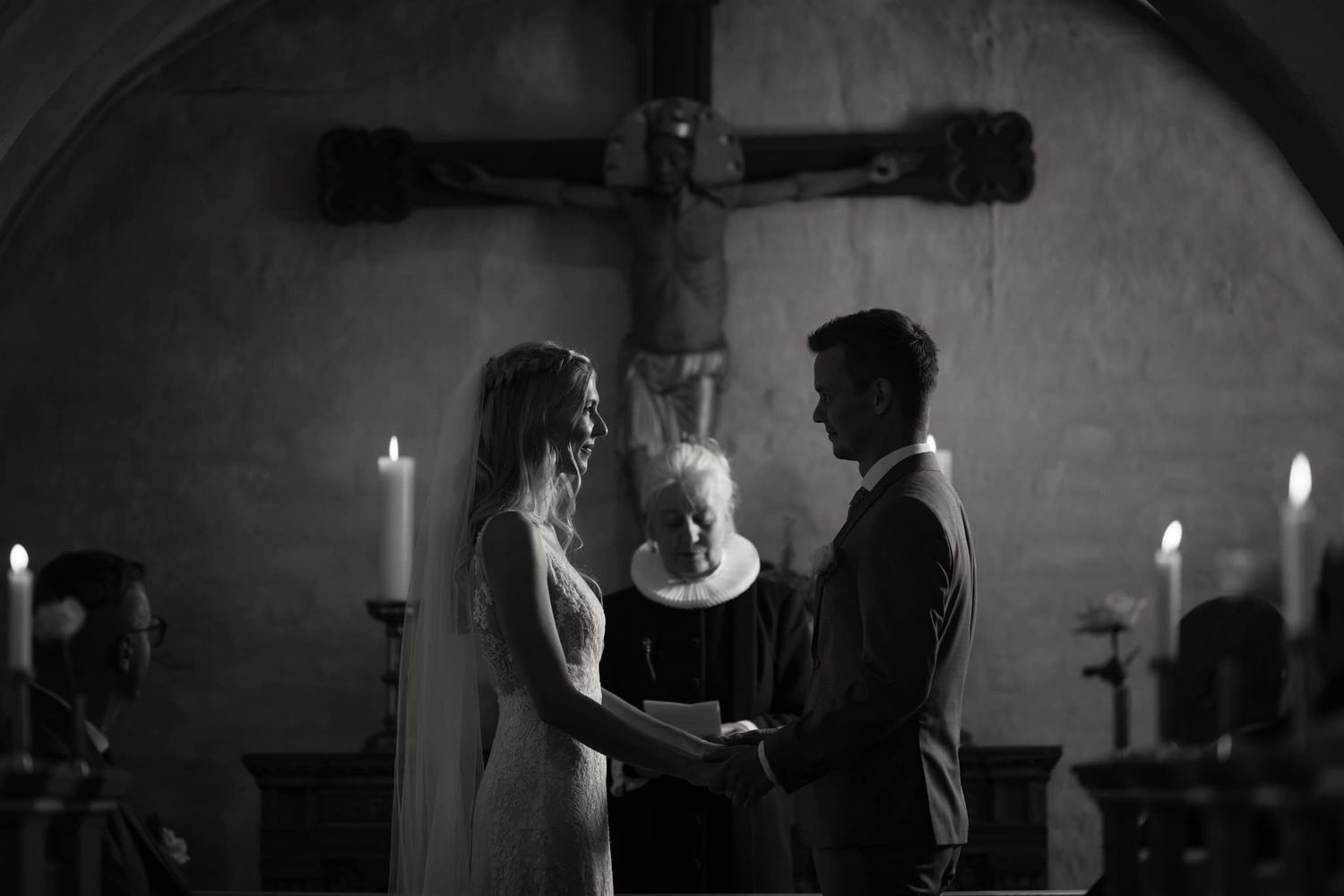 Black and white church interior with lit candles and gothic architecture creating a solemn atmosphere.