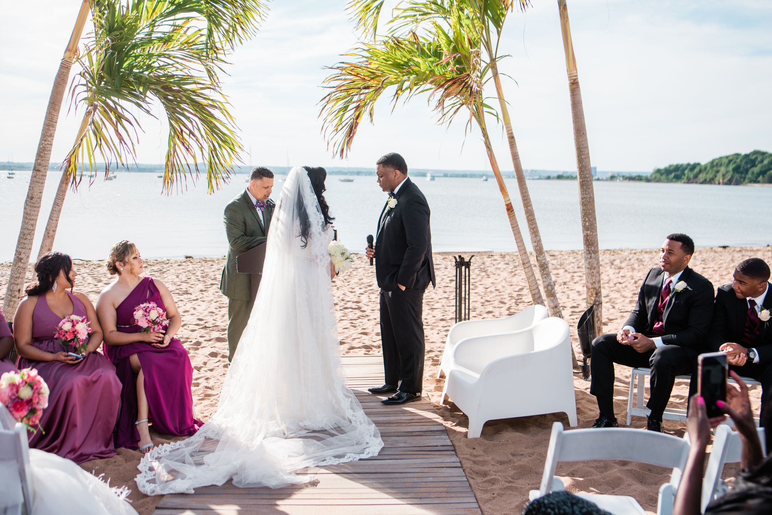 Beach wedding ceremony setup with palm trees, white chairs and ocean view.