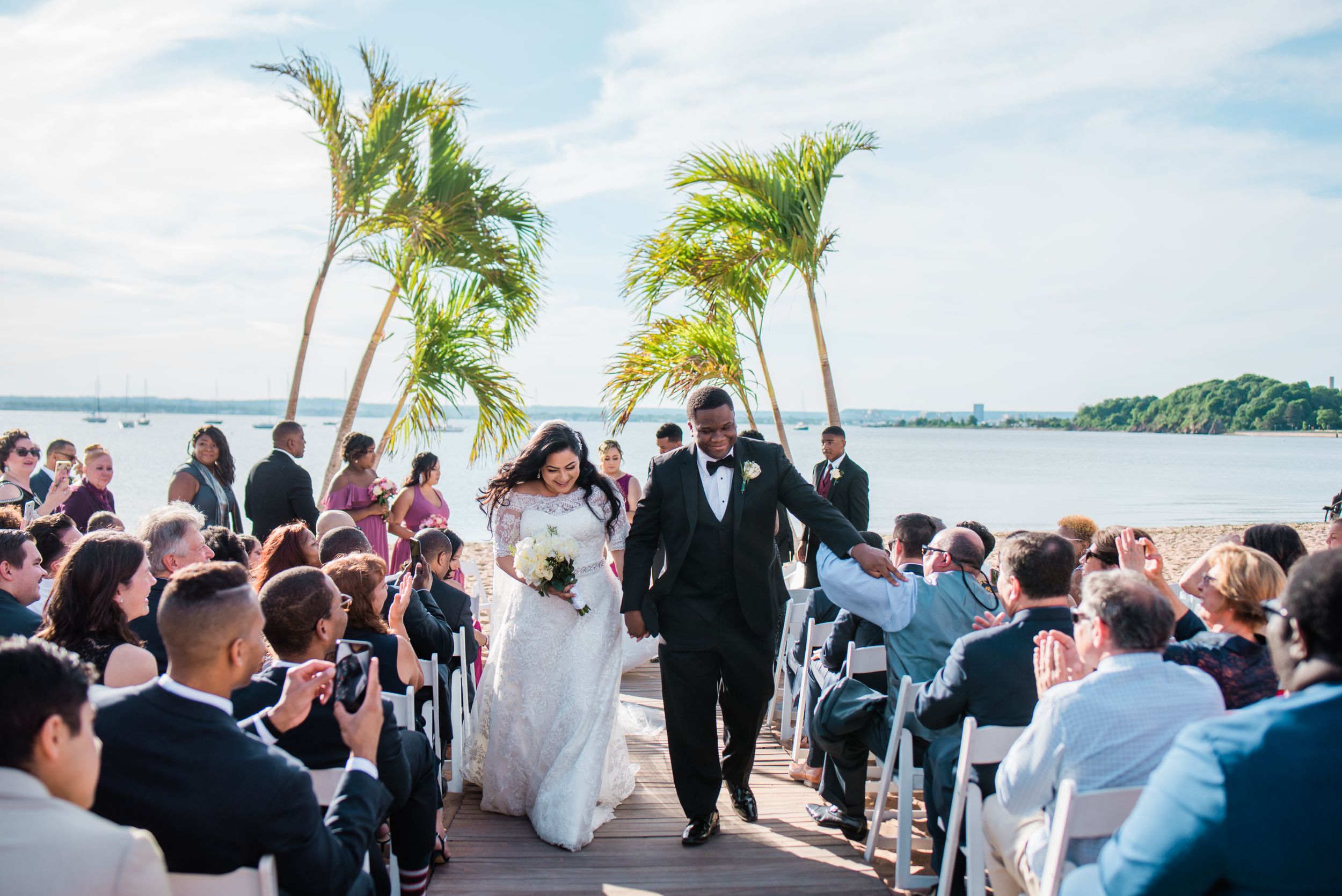 Wedding couple walks back down aisle as newlyweds while guests celebrate on waterfront at Anthonys Ocean View