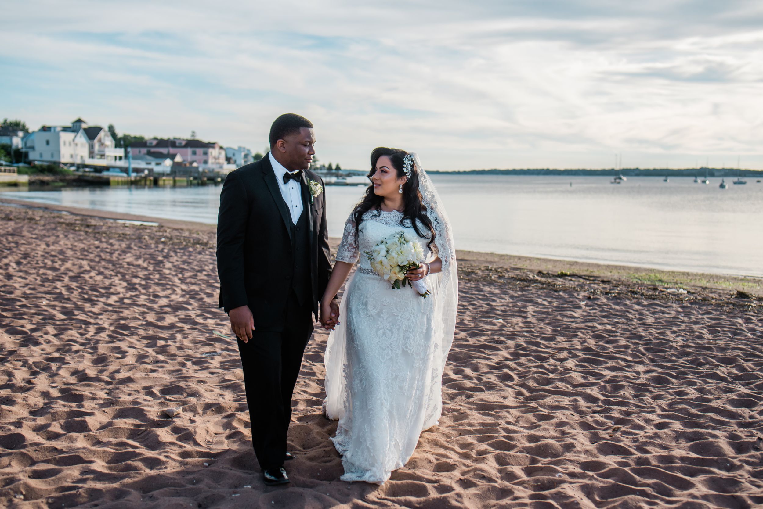 Newlywed couple walks together on beach shore during sunset portrait session.