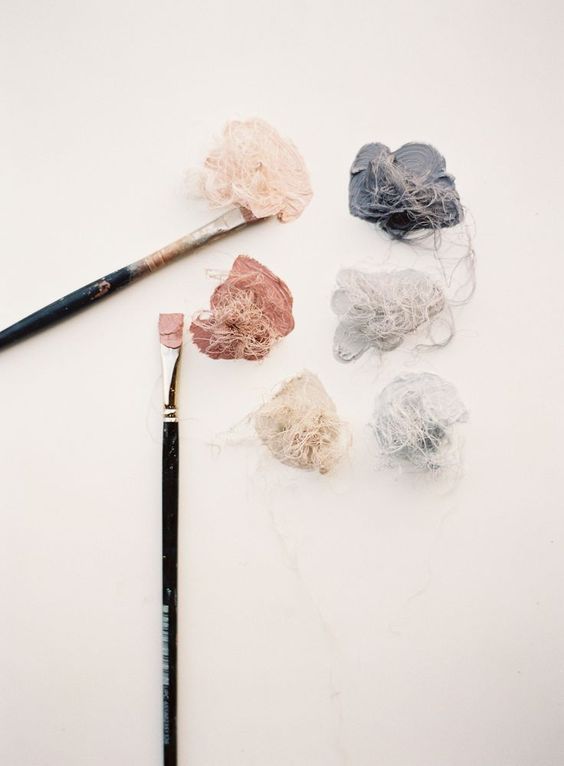 Art supplies and crumpled fabric swatches in soft pink and grey tones with paint brushes.