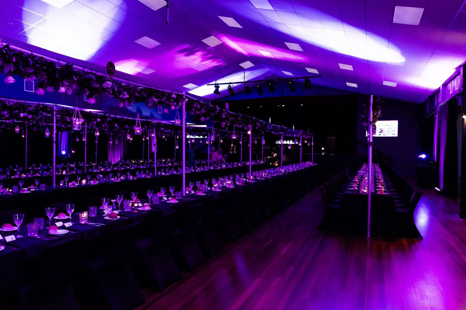 Elegant event space with purple lighting and long tables set for dining.