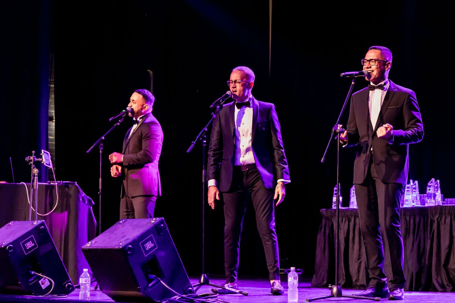 Male vocal group performing on stage in formal attire under stage lights.