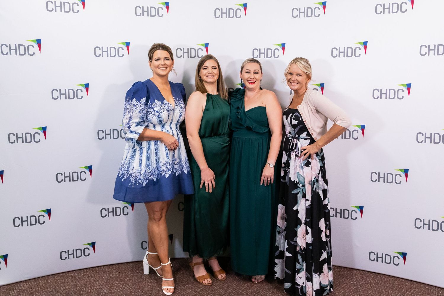 Group photo at CHDC event backdrop wearing formal attire including blue and green dresses.