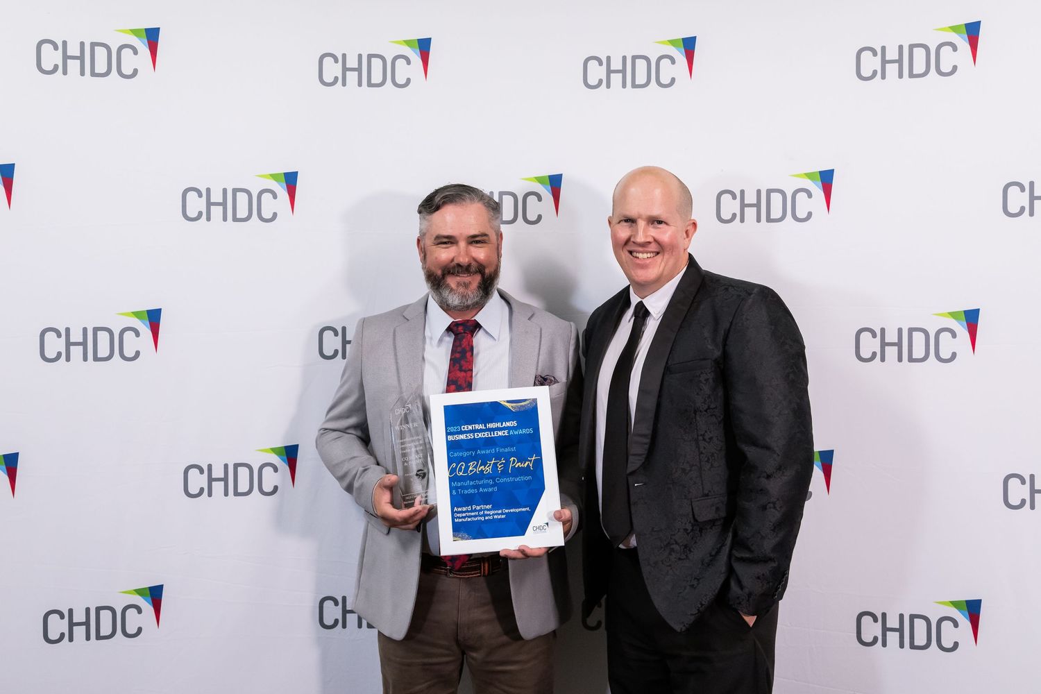 Two men in business attire pose with award certificate against CHDC backdrop.