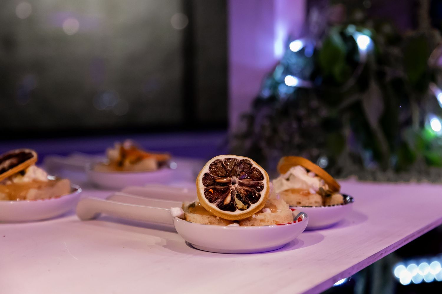 Elegant plated dessert with dried citrus garnish in purple ambient lighting.