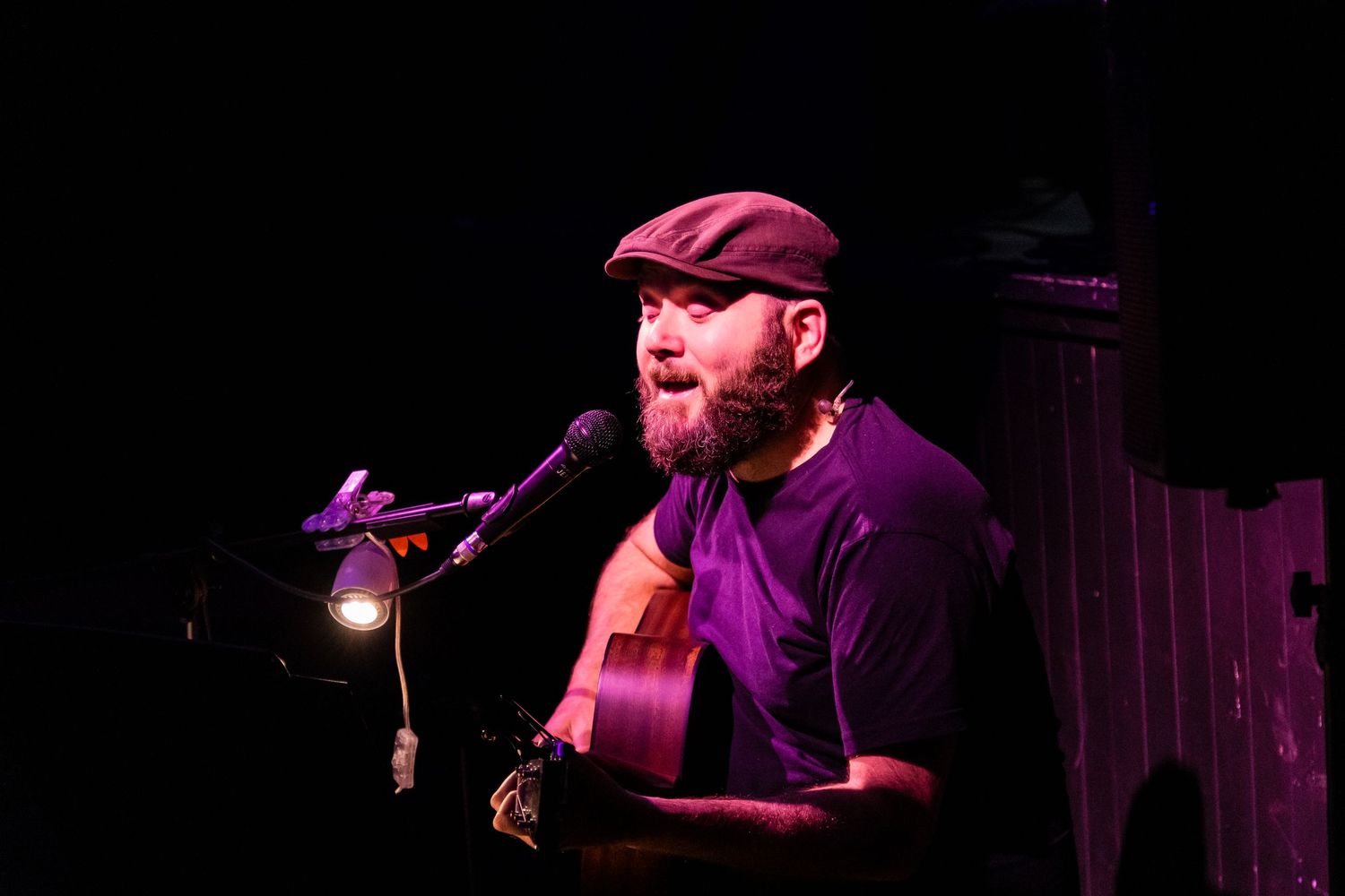 Musician performing with acoustic guitar on dark stage with spotlight.