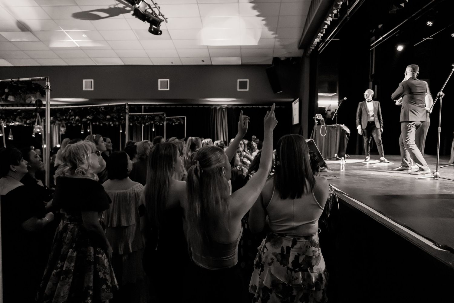 Black and white photo of audience members raising hands during performance.
