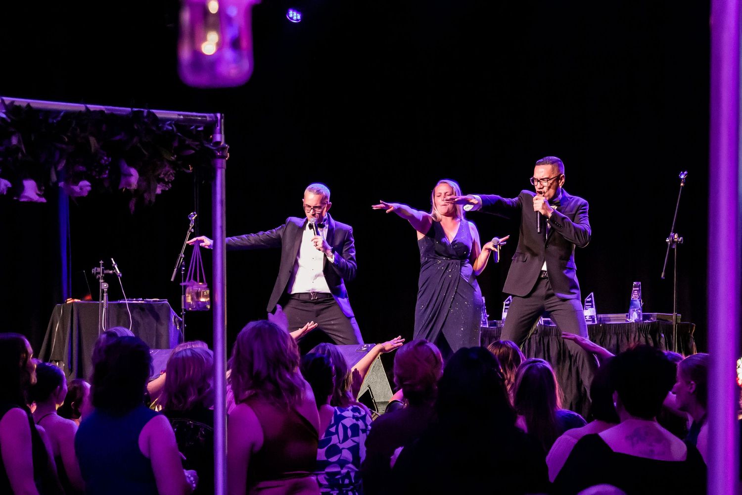 Performers on stage entertaining crowd in purple-lit concert venue.