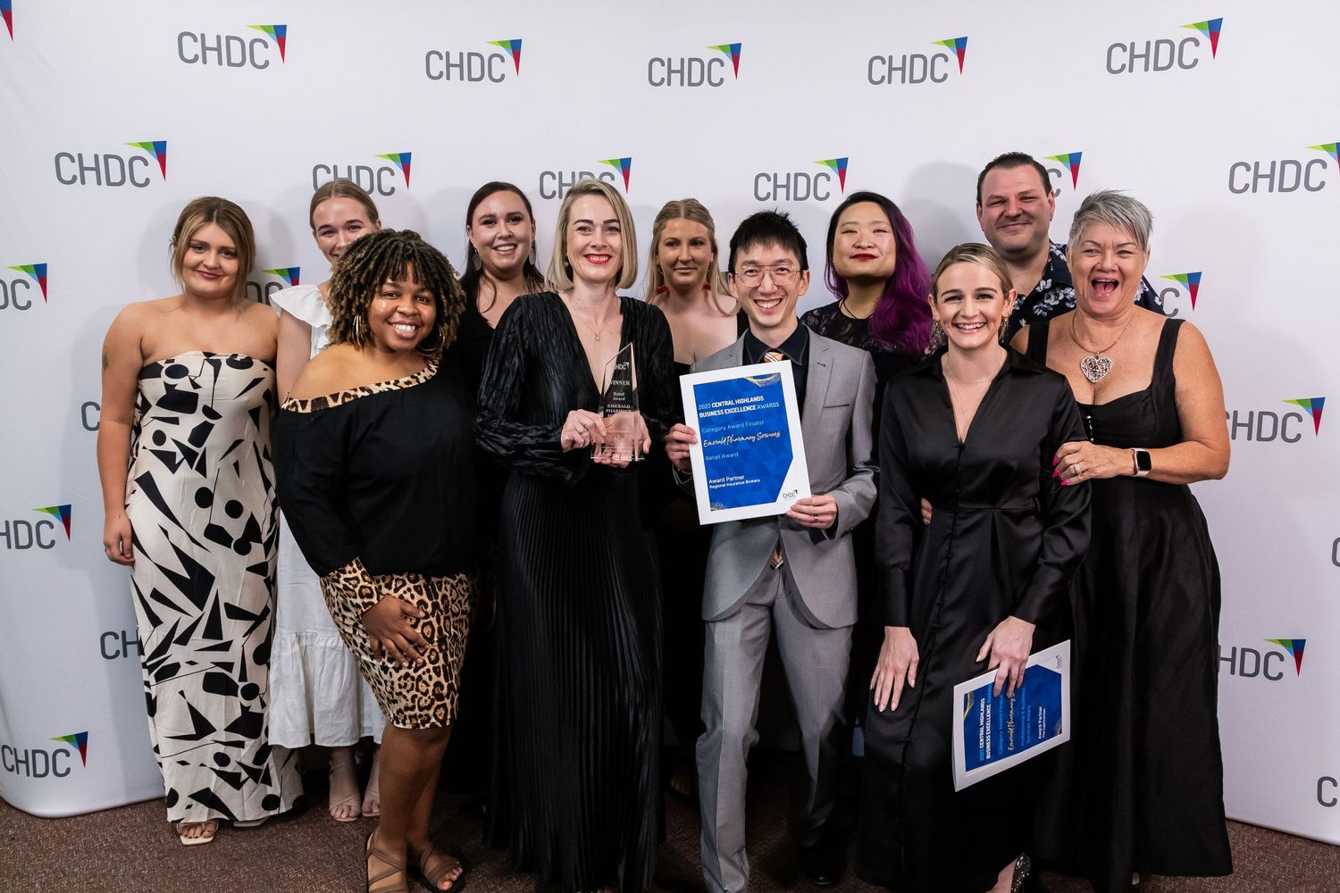 A group celebrating at an awards ceremony posing with blue certificates against a CHDC branded backdrop.
