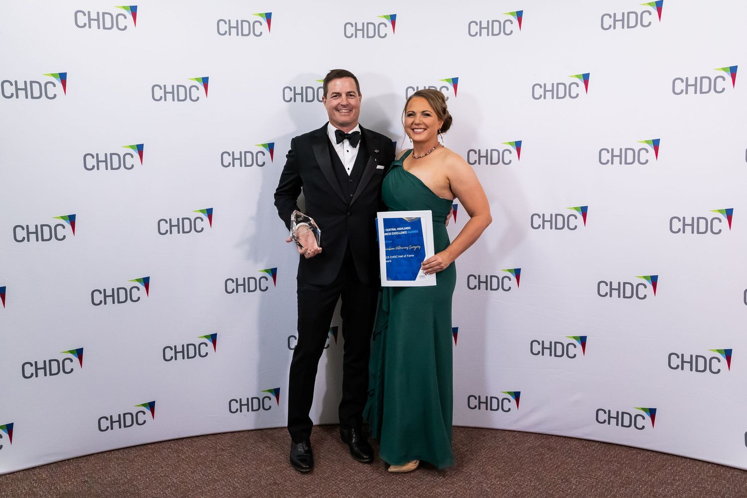 Award winners in formal evening wear holding a blue certificate at CHDC event.