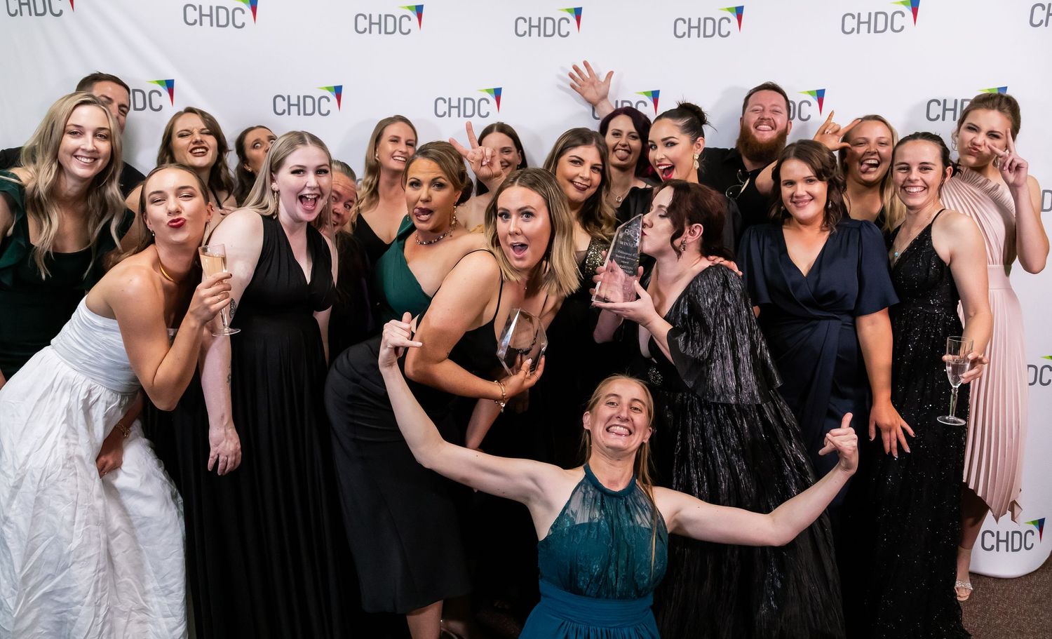 Large group in formal dresses and suits celebrating together at an awards event.